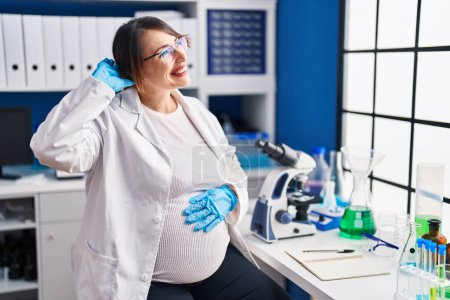 Photo for Pregnant woman working at scientist laboratory smiling confident touching hair with hand up gesture, posing attractive and fashionable - Royalty Free Image