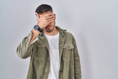 Téléchargez les photos : Young hispanic man standing over isolated background covering eyes with hand, looking serious and sad. sightless, hiding and rejection concept - en image libre de droit