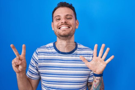 Photo for Young hispanic man standing over blue background showing and pointing up with fingers number seven while smiling confident and happy. - Royalty Free Image