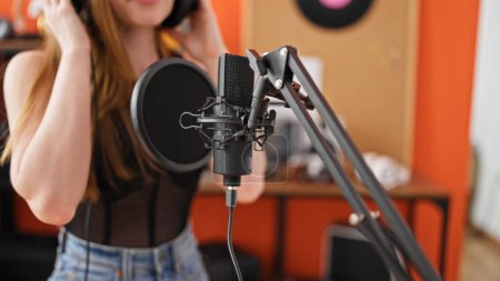 Photo for Young blonde woman musician wearing headphones singing song at music studio - Royalty Free Image
