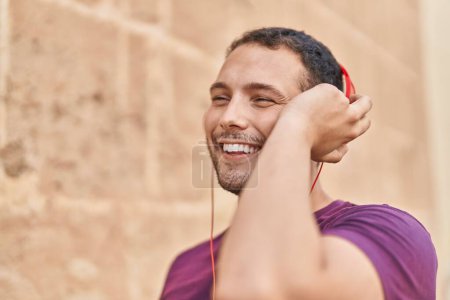 Téléchargez les photos : Jeune homme souriant confiant écoutant de la musique sur fond de briques isolées - en image libre de droit