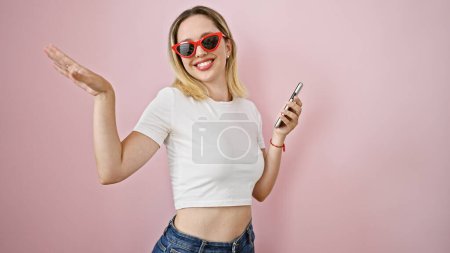 Foto de Mujer rubia joven bailando escuchando música en un smartphone sobre un fondo rosa aislado - Imagen libre de derechos