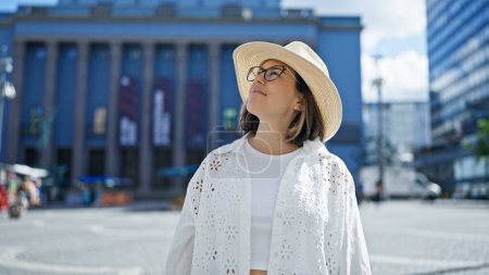 Téléchargez les photos : Belle jeune femme hispanique souriante confiante regardant vers le côté portant un chapeau d'été à la construction du prix Nobel - en image libre de droit