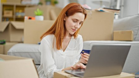 Photo for Young redhead woman shopping with laptop and credit card sitting on floor at new home - Royalty Free Image