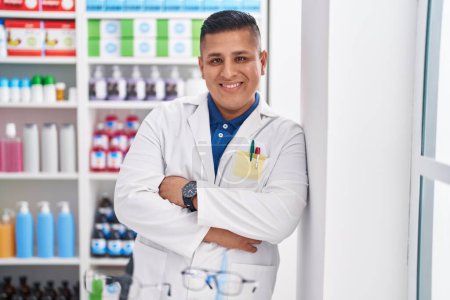 Téléchargez les photos : Young latin man pharmacist smiling confident standing with arms crossed gesture at pharmacy - en image libre de droit