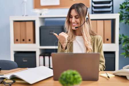 Photo for Young hispanic woman wearing call center agent headset working at the office pointing thumb up to the side smiling happy with open mouth - Royalty Free Image
