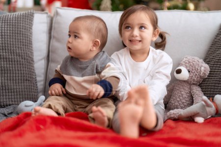 Téléchargez les photos : Frère et sœur souriants confiants assis sur le canapé près de l'arbre de Noël à la maison - en image libre de droit