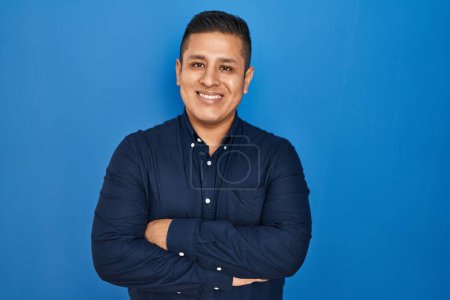 Téléchargez les photos : Jeune homme hispanique debout sur fond bleu heureux visage souriant avec les bras croisés regardant la caméra. personne positive. - en image libre de droit