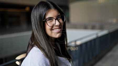 Téléchargez les photos : Jeune belle femme hispanique portant des lunettes souriant heureux au bureau - en image libre de droit