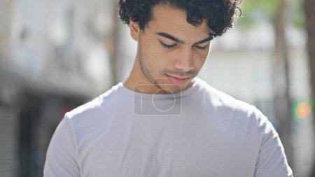 Téléchargez les photos : Jeune homme latin regardant vers le bas avec une expression sérieuse à la rue - en image libre de droit
