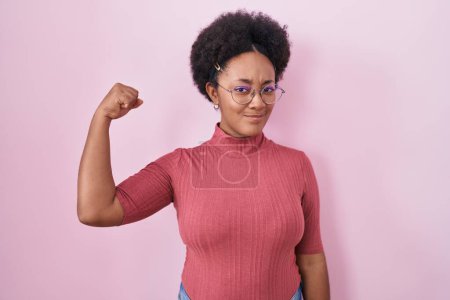 Foto de Hermosa mujer africana con el pelo rizado de pie sobre el fondo rosa persona fuerte que muestra el músculo del brazo, confiado y orgulloso de poder - Imagen libre de derechos