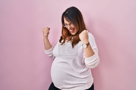 Photo for Pregnant woman standing over pink background very happy and excited doing winner gesture with arms raised, smiling and screaming for success. celebration concept. - Royalty Free Image