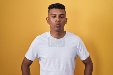 Photo for Young hispanic man standing over yellow background making fish face with lips, crazy and comical gesture. funny expression. - Royalty Free Image
