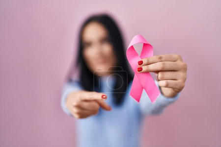 Foto de Mujer hispana sosteniendo cinta de cáncer rosa sonriendo feliz señalando con la mano y el dedo - Imagen libre de derechos