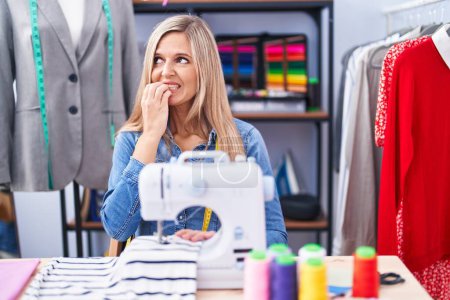 Photo for Blonde woman dressmaker designer using sew machine looking stressed and nervous with hands on mouth biting nails. anxiety problem. - Royalty Free Image