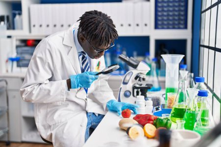 Téléchargez les photos : Homme scientifique afro-américain à la recherche de tomate en utilisant loupe au laboratoire - en image libre de droit