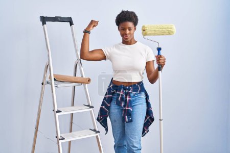 Foto de Afro-americana mujer sosteniendo rodillo pintor fuerte persona mostrando brazo músculo, confiado y orgulloso de poder - Imagen libre de derechos