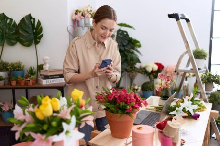 Foto de Joven florista mujer caucásica hacer foto para plantar por teléfono inteligente en la tienda de flores - Imagen libre de derechos