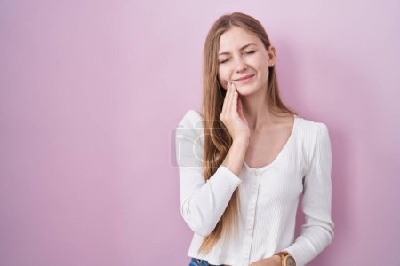 Téléchargez les photos : Young caucasian woman standing over pink background touching mouth with hand with painful expression because of toothache or dental illness on teeth. dentist - en image libre de droit