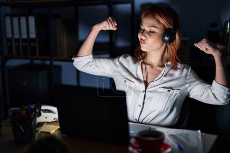 Téléchargez les photos : Young caucasian woman working at the office at night showing arms muscles smiling proud. fitness concept. - en image libre de droit