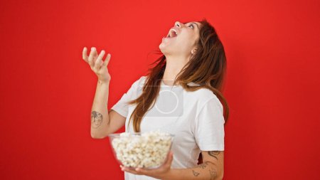 Téléchargez les photos : Jeune belle femme hispanique mangeant du pop-corn riant beaucoup sur fond rouge isolé - en image libre de droit