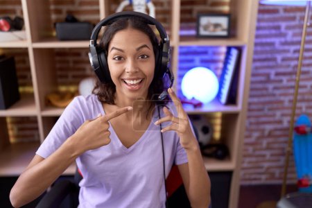 Photo for Young hispanic woman playing video games wearing headphones smiling happy pointing with hand and finger - Royalty Free Image