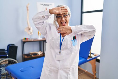 Photo for Middle age woman with grey hair working at pain recovery clinic smiling cheerful playing peek a boo with hands showing face. surprised and exited - Royalty Free Image