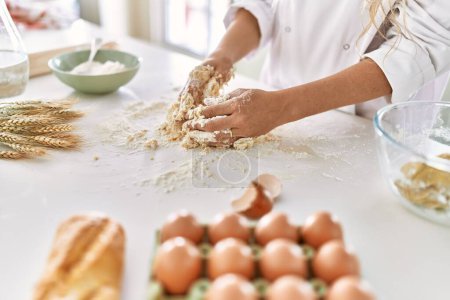Téléchargez les photos : Young woman wearing cook uniform kneading flour at kitchen - en image libre de droit