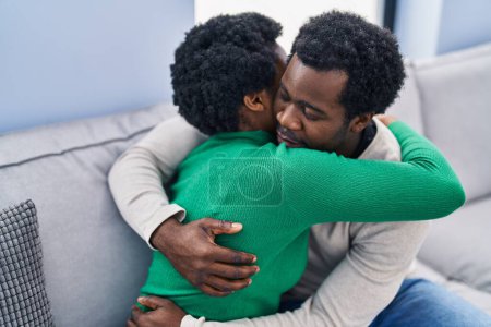 Foto de Africano americano hombre y mujer pareja abrazándose uno al otro sentado en sofá en casa - Imagen libre de derechos