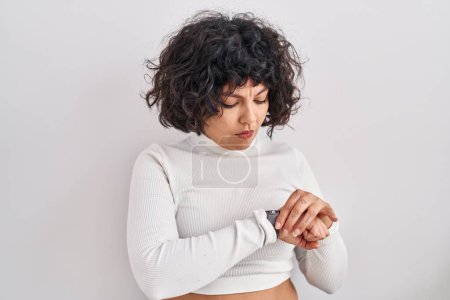 Foto de Mujer hispana con el pelo rizado de pie sobre fondo aislado comprobar el tiempo en reloj de pulsera, relajado y seguro - Imagen libre de derechos
