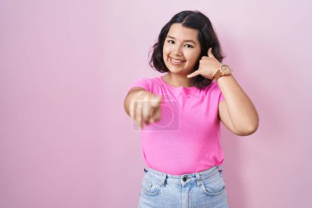 Téléchargez les photos : Jeune femme hispanique debout sur fond rose souriant faire parler au téléphone geste et vous pointant du doigt. Appelle-moi. - en image libre de droit