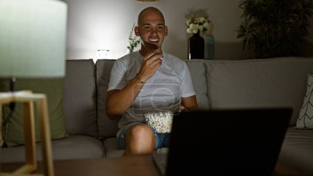 Téléchargez les photos : Young hispanic man watching movie eating popcorn at home - en image libre de droit