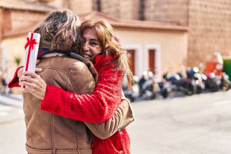 Téléchargez les photos : Deux femmes mère et fille étreignant l'autre surprise avec un cadeau dans la rue - en image libre de droit