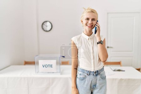 Téléchargez les photos : Jeune femme blonde parlant sur smartphone souriant au collège électoral - en image libre de droit