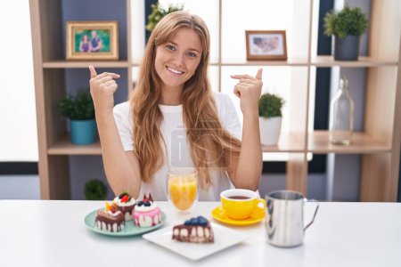 Foto de Joven mujer caucásica comiendo pasteles t para el desayuno mirando confiado con sonrisa en la cara, señalándose con los dedos orgullosos y felices. - Imagen libre de derechos