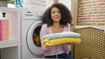 Téléchargez les photos : Femme afro-américaine laver les vêtements tenant des serviettes pliées à la buanderie - en image libre de droit