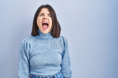 Téléchargez les photos : Young hispanic woman standing over blue background angry and mad screaming frustrated and furious, shouting with anger. rage and aggressive concept. - en image libre de droit