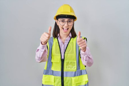 Téléchargez les photos : Fille hispanique portant uniforme constructeur et casque de sécurité approuvant faire un geste positif avec la main, pouces levés souriant et heureux pour le succès. geste gagnant. - en image libre de droit