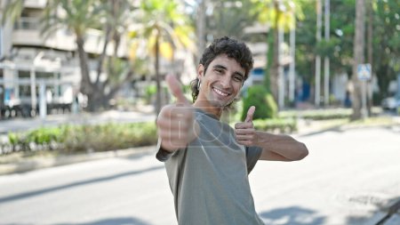 Foto de Young hispanic man smiling confident doing ok sign with thumbs up at street - Imagen libre de derechos