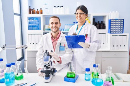 Téléchargez les photos : Deux jeunes gens travaillant au laboratoire scientifique regardant positif et heureux debout et souriant avec un sourire confiant montrant des dents - en image libre de droit