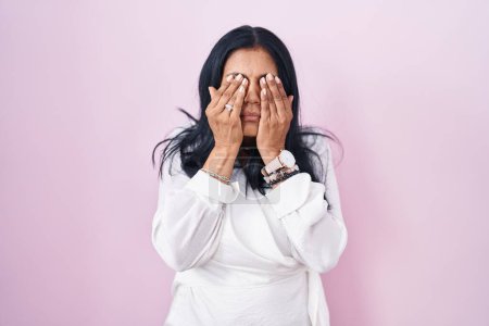 Foto de Mujer hispana madura de pie sobre fondo rosa frotando los ojos para la fatiga y el dolor de cabeza, la expresión somnolienta y cansada. problema de visión - Imagen libre de derechos