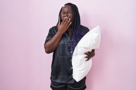 Photo for Young african woman wearing pijama hugging pillow bored yawning tired covering mouth with hand. restless and sleepiness. - Royalty Free Image