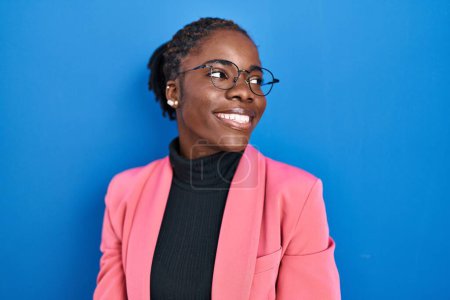 Foto de Beautiful black woman standing over blue background looking away to side with smile on face, natural expression. laughing confident. - Imagen libre de derechos