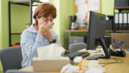 Foto de Mujer de mediana edad trabajadora de negocios usando la computadora estornudando en la oficina - Imagen libre de derechos