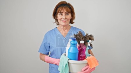 Foto de Mujer de mediana edad limpiador profesional cesta con productos limpios sobre fondo blanco aislado - Imagen libre de derechos