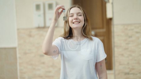 Téléchargez les photos : Young caucasian woman smiling confident holding key of new home at street - en image libre de droit