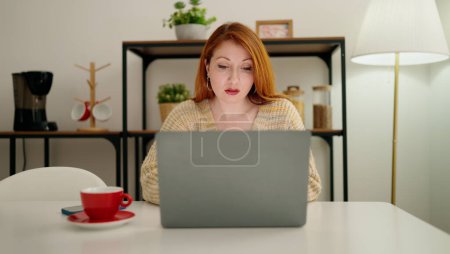 Téléchargez les photos : Jeune rousse femme utilisant un ordinateur portable boire du café à la maison - en image libre de droit