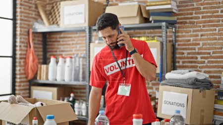 Téléchargez les photos : Jeune homme hispanique bénévole parlant sur smartphone au centre de charité - en image libre de droit