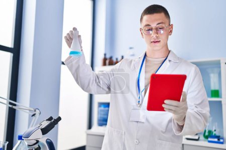 Téléchargez les photos : Jeune homme hispanique scientifique mesurant le liquide à l'aide d'un pavé tactile au laboratoire - en image libre de droit