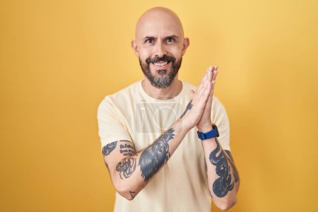 Téléchargez les photos : Homme hispanique avec des tatouages debout sur fond jaune applaudissements heureux et joyeux, souriant mains fières ensemble - en image libre de droit